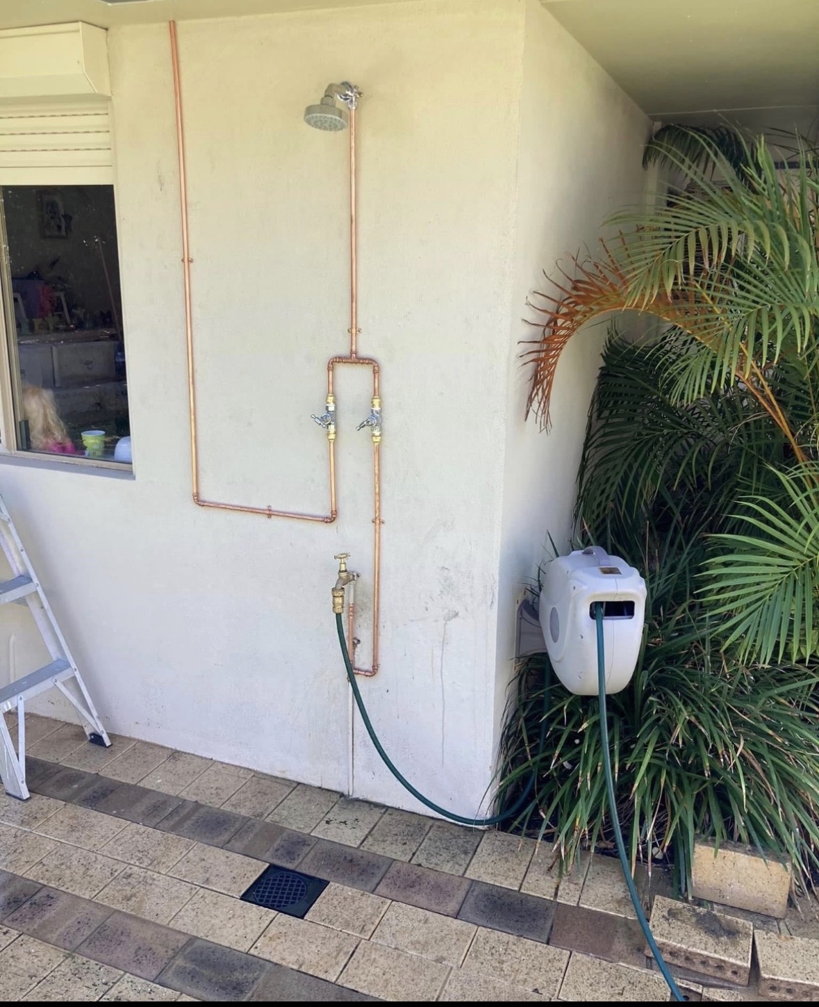 Outdoor copper pipe shower installed on exterior render wall with tap and hose connection