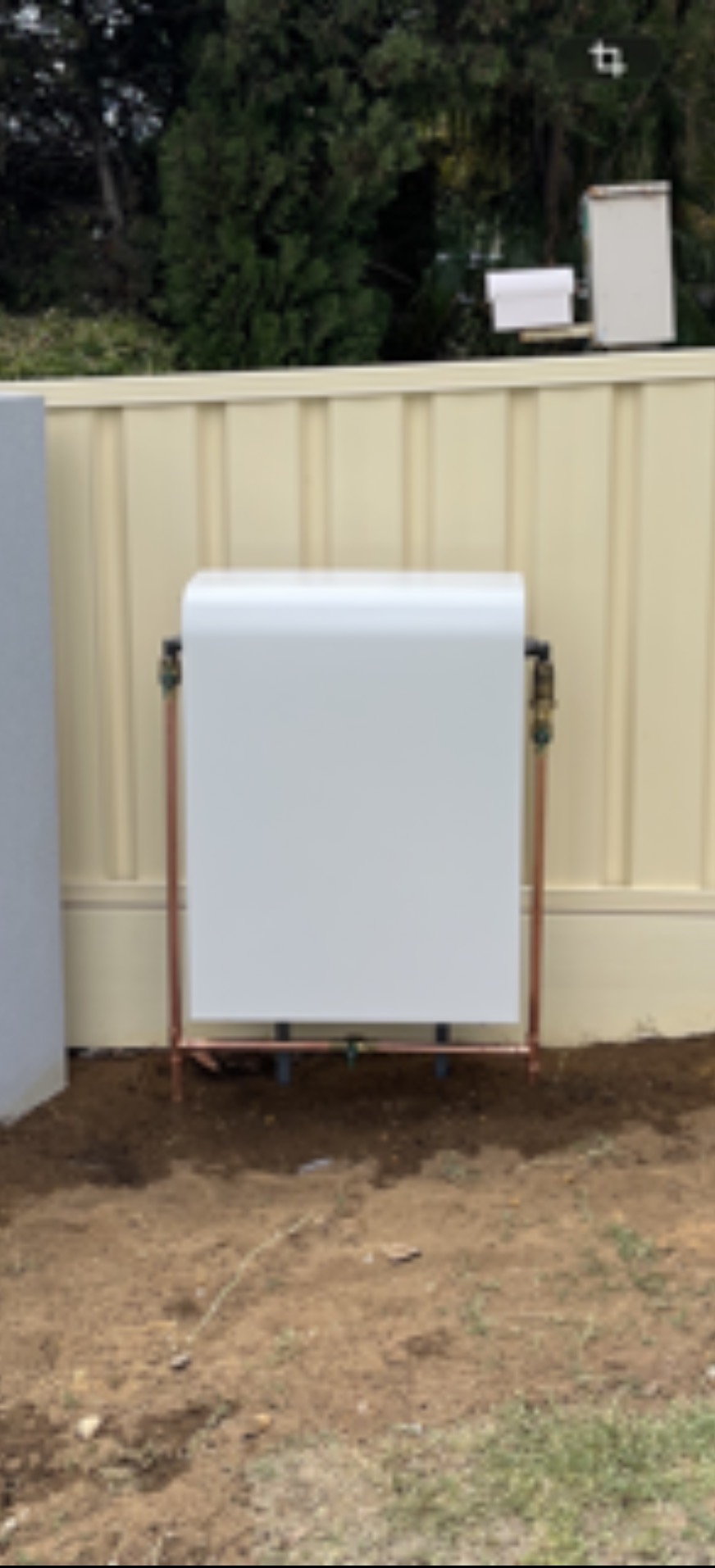 New hot water unit installed against fence with copper pipe connections